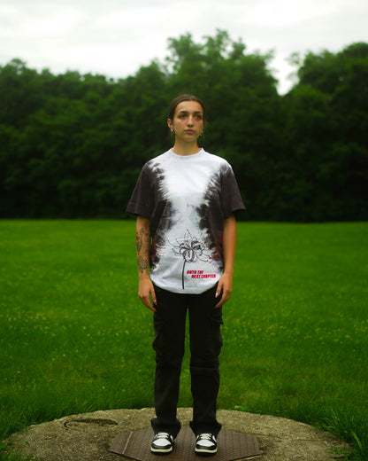 Person wearing a tie-dye shirt with a graphic design in a grassy outdoor setting